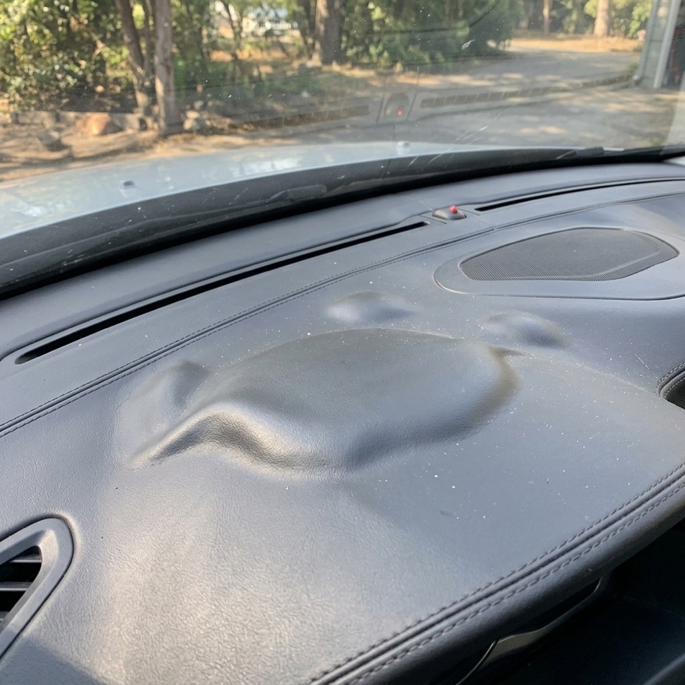Black dashboard leather lifted into a bubble near the windshield