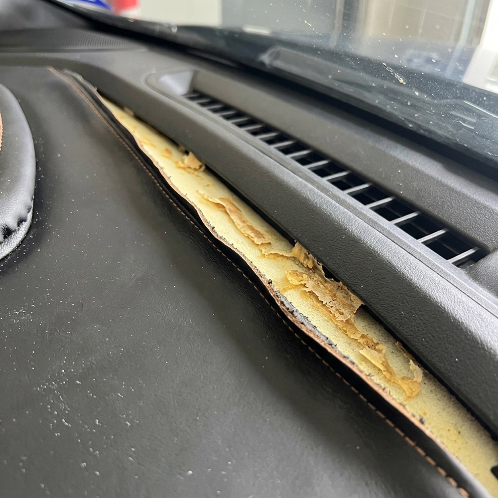 Dashboard leather pulled back from an air vent, with the yellow foam showing