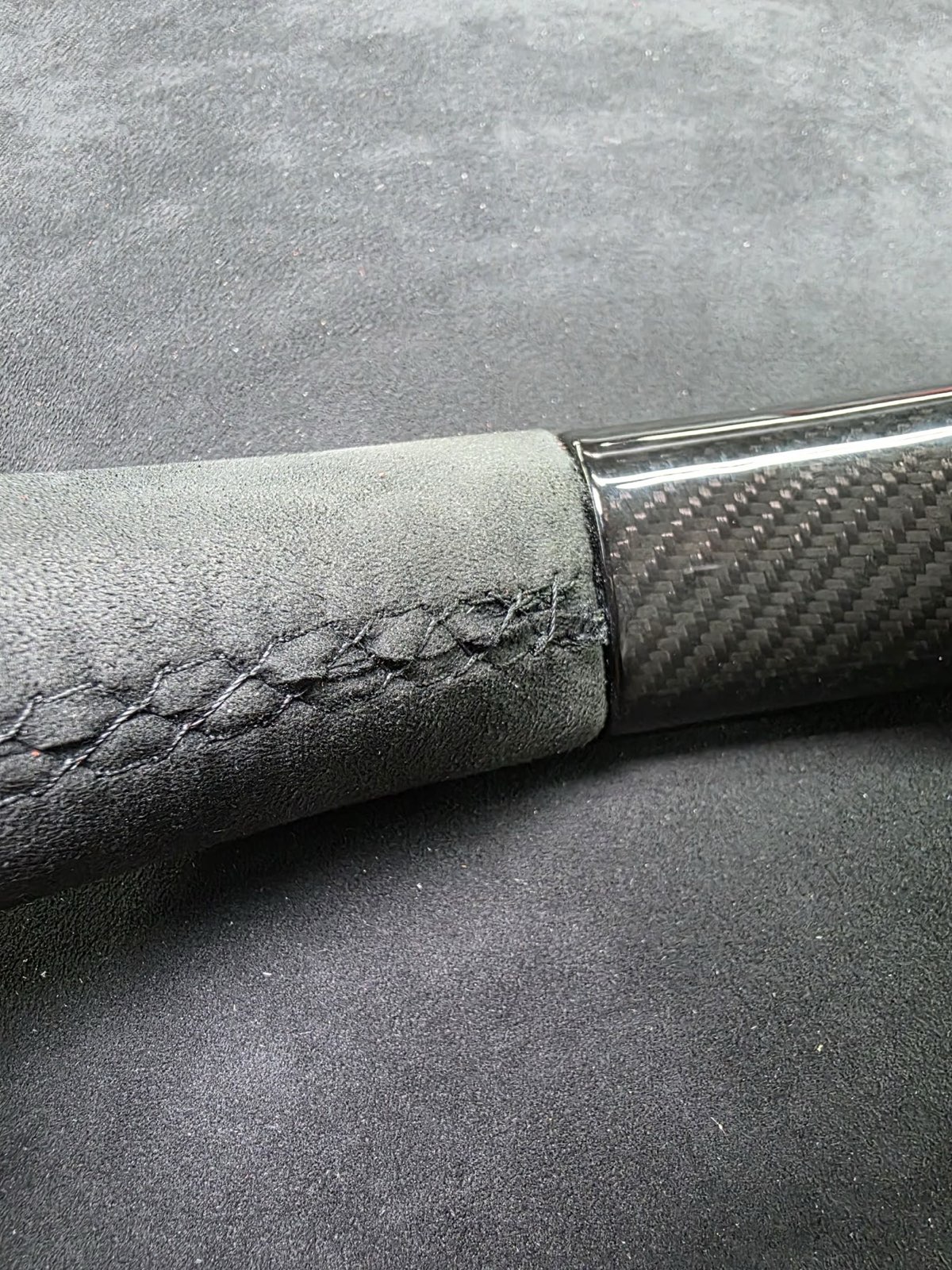 Grey Alcantara on a steering wheel grip, matted and shiny where the hands hold it, next to a carbon section