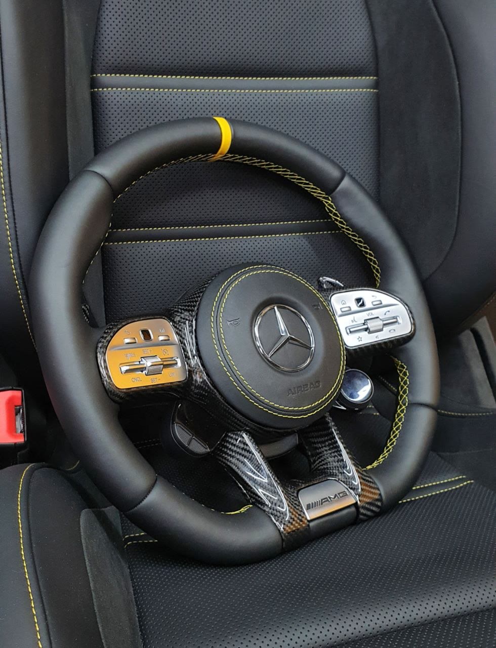 A black AMG steering wheel with yellow stitching and a yellow zero mark