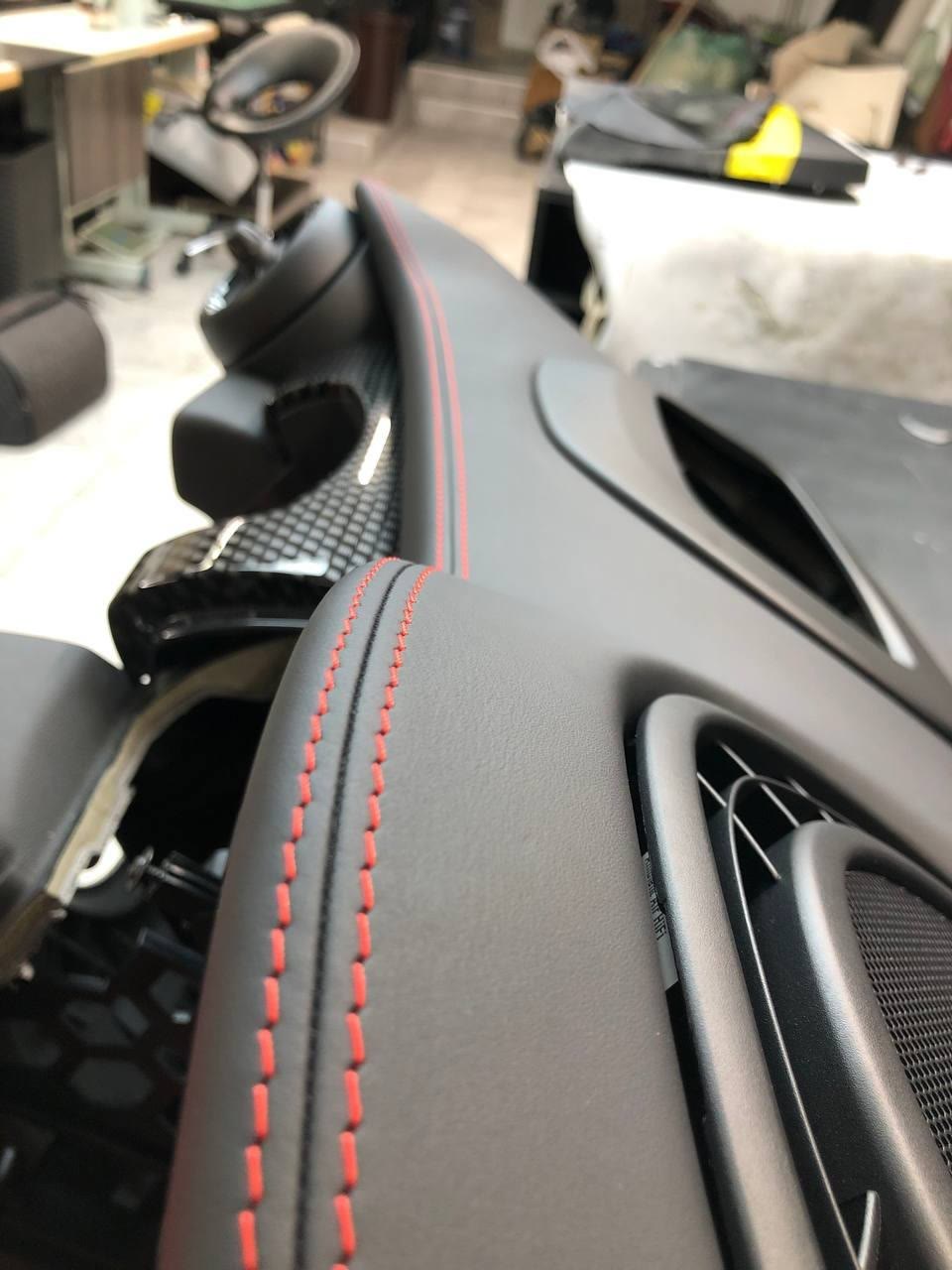 A black leather dashboard with red stitching next to carbon trim
