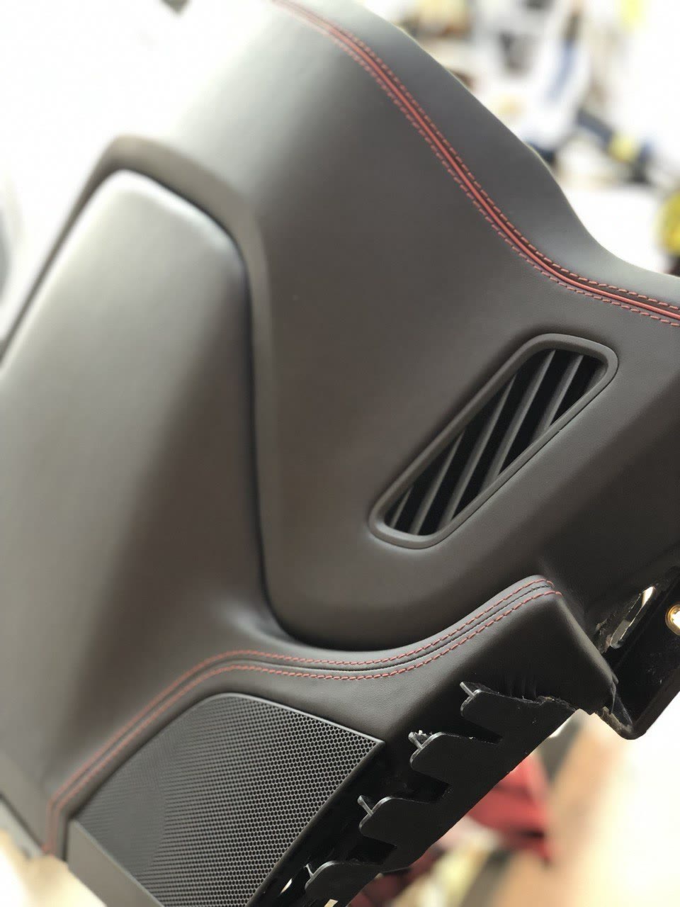 A dashboard in black leather with red double stitching around the air vent