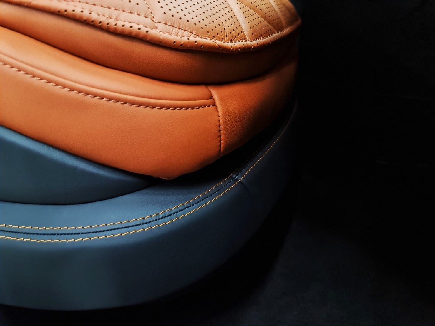 A car seat in tan and teal leather joined with a yellow stitch